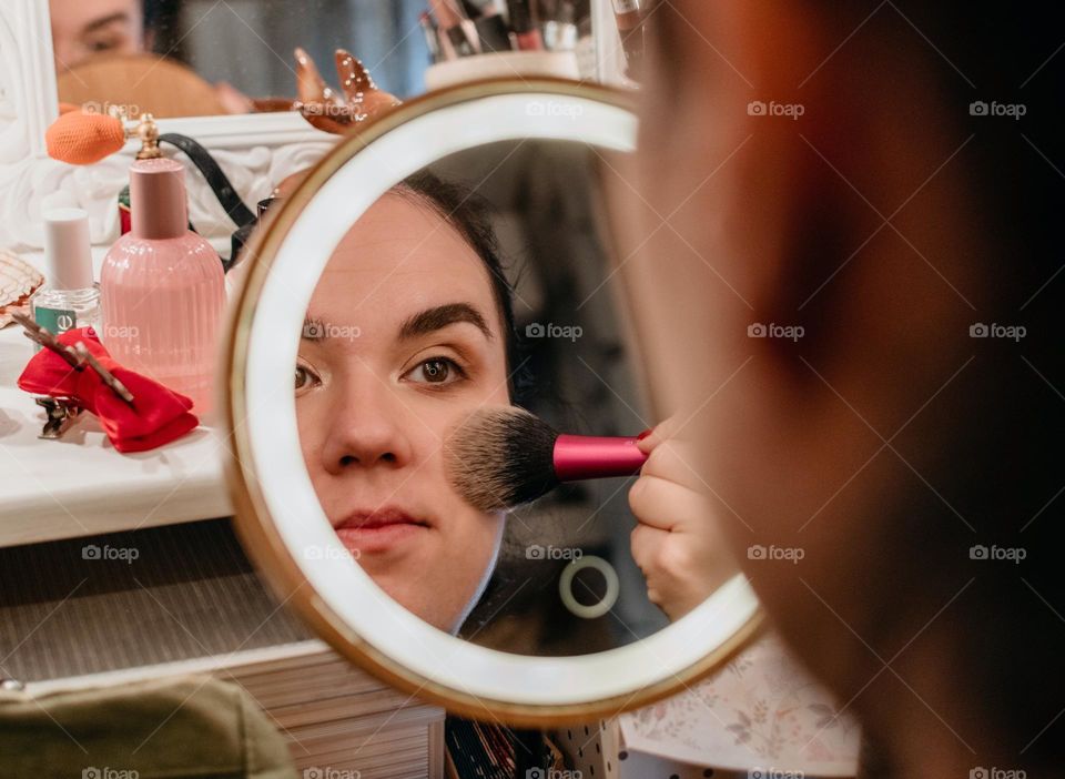 Portrait of young woman doing her make-up in front of circular led illuminated mirror