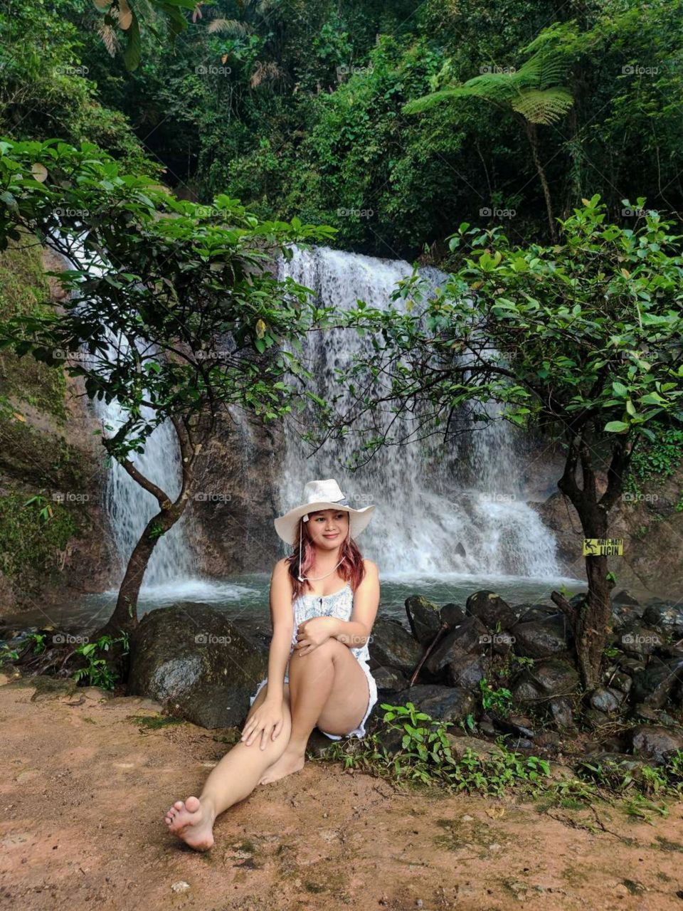 Portrait of a young woman in a hat sitting in front of a waterfall in the middle of the forest