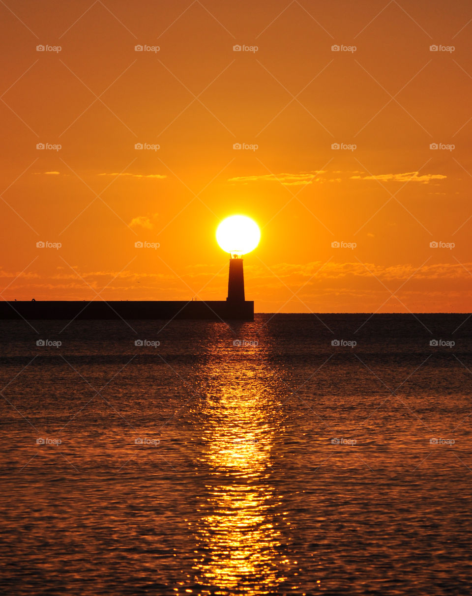 sun above the lighthouse during golden sunrise over the baltic sea in Gdynia, Poland