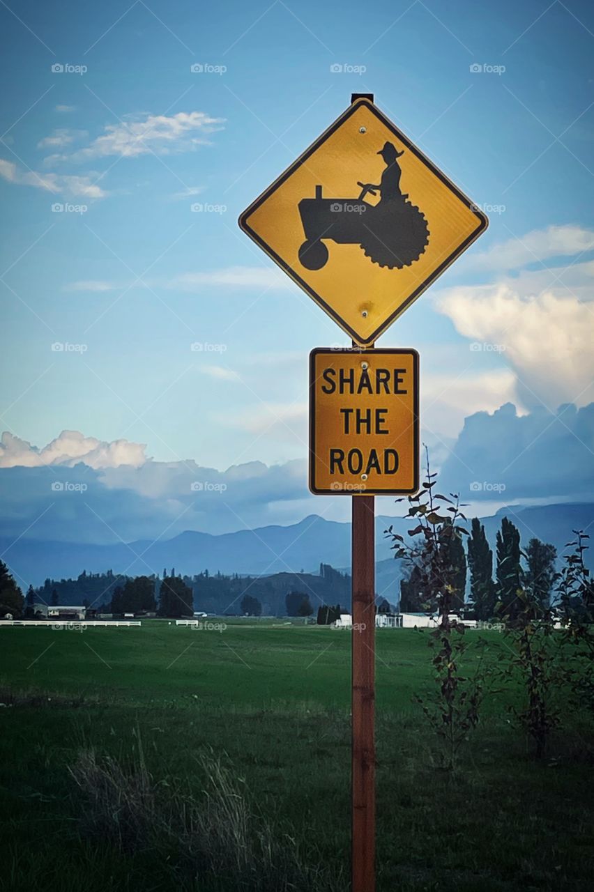 A road sign stands on the corner of a rural field, a friendly reminder that not all vehicles are cars.