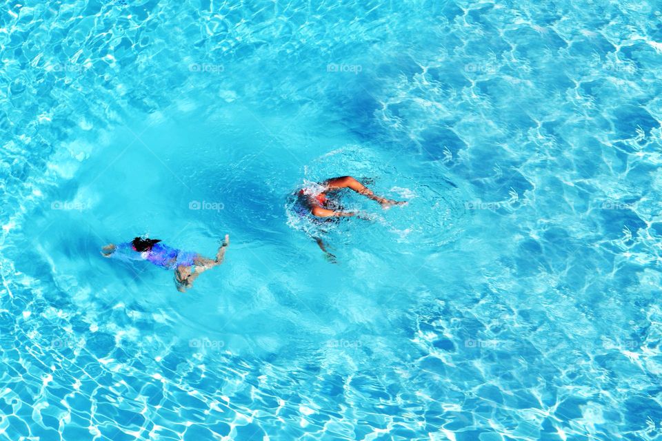 Two sisters on vacation enjoy a hot days worth of swimming in an emerald blue pool.