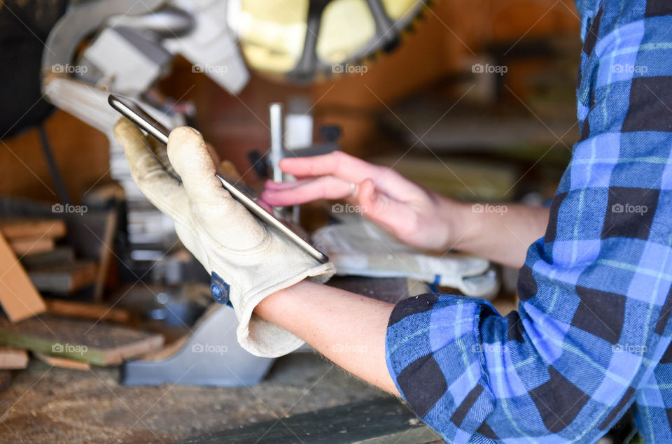 Person using a tablet while working with wood and saw at a workbench