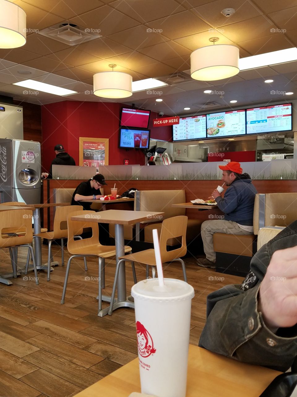 Inside a fast food restaurant, people eating, booths & tables with get your own drinks area.