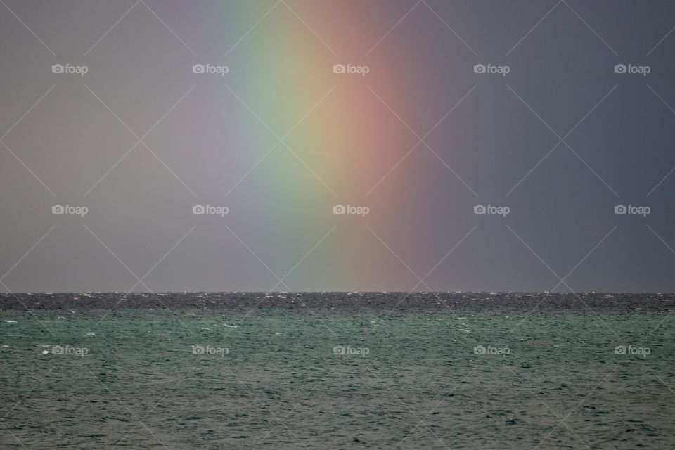 Colourful rainbow arching through dark stormy sky into ocean horizon