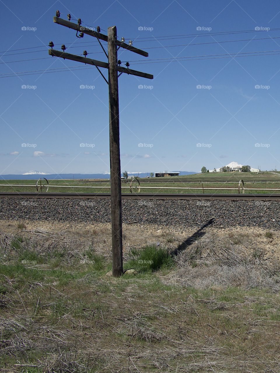 Old wooden telephone poles next to railroad tracks with the Cascade Mountains in the background on a beautiful sunny spring morning in rural Central Oregon. 