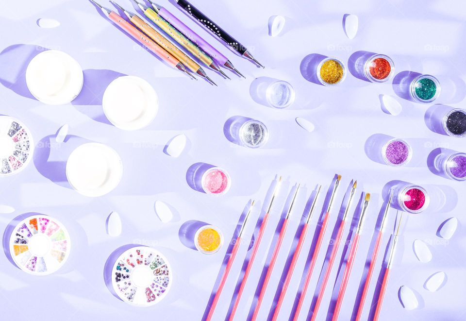 Set of different brushes,sticks,glitter nails,gel nail polish,false nails and rhinestones on lilac background,flat lay. Concept cosmetics and beauty salons.