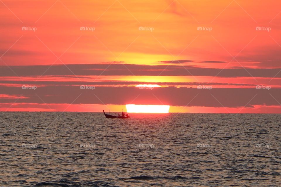 A long tail boat drifting by as the sun sets in Phuket Thailand. Surin beach.