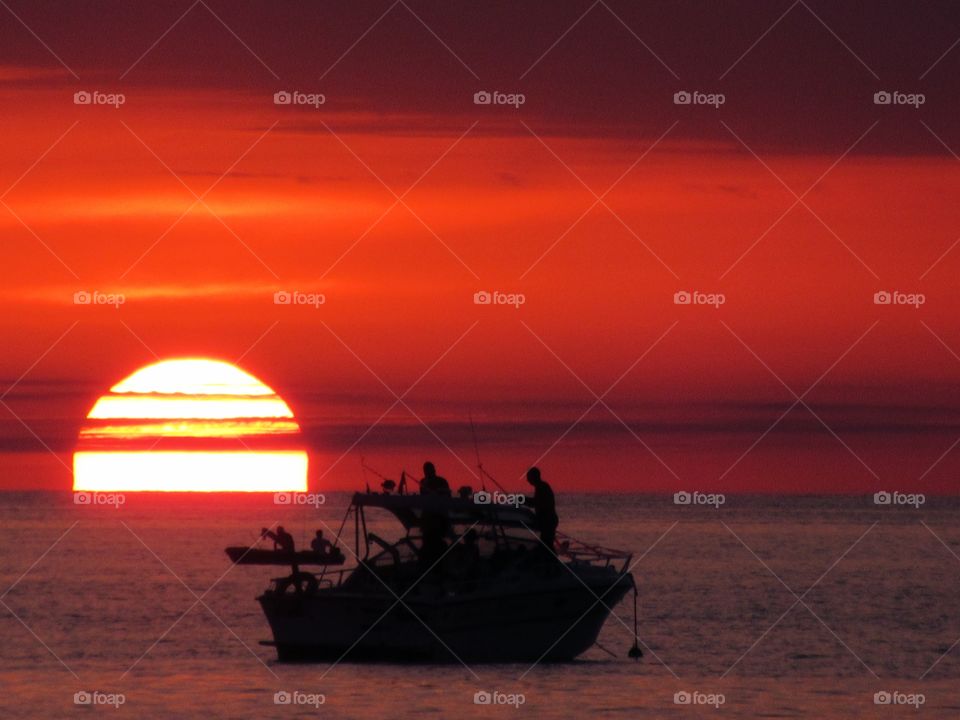Silhouetted people on boats in sea during sunset