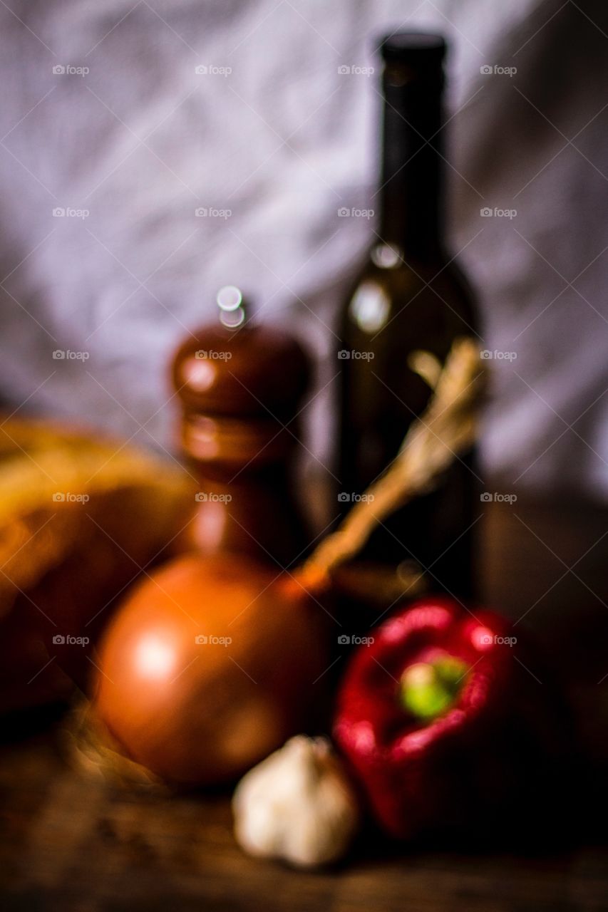 Stylized Herbs. Olive oil, pepper grinder, onion, red bell pepper, garlic, and loaf of bread on wooden cutting board.