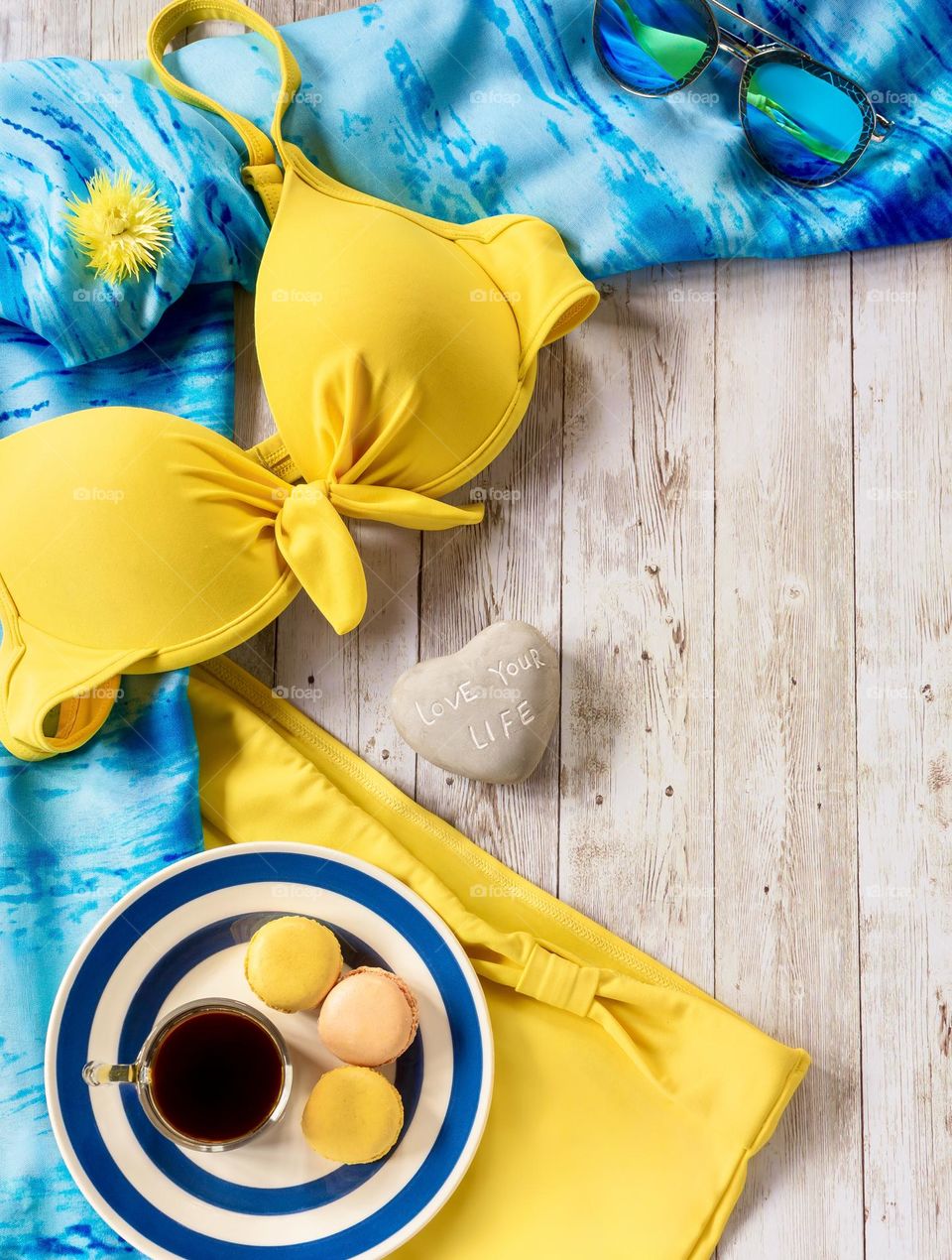Swimwear flat lay in blue & yellow, with coffee and macaroons.