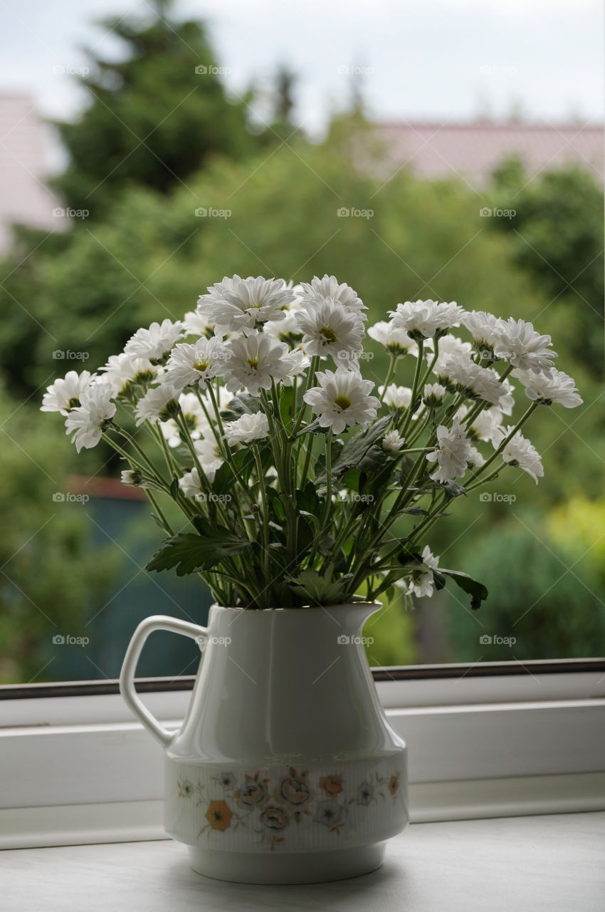 Bouquet of white flowers in a jug on the window