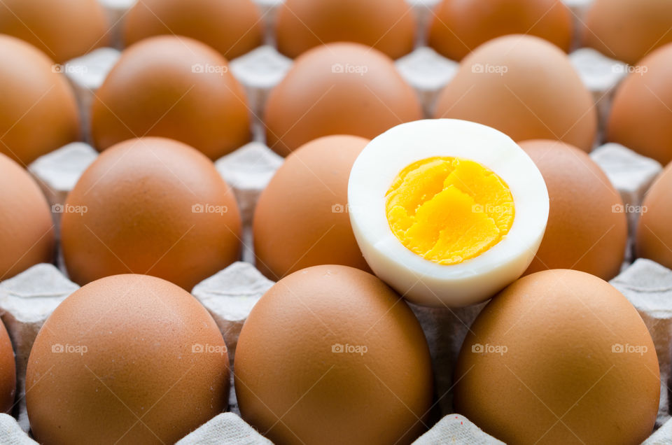 Boiled chicken egg placed on raw egg. Group of fresh eggs in paper tray.