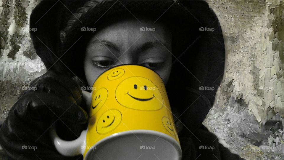 Woman holding a smiling face mug while wearing black gloves.