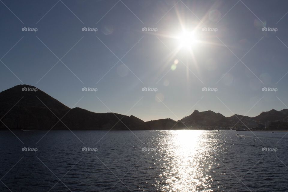 Setting sun glimmering on the sea with rocky cliffs in the distance in Cabo San Lucas, Mexico