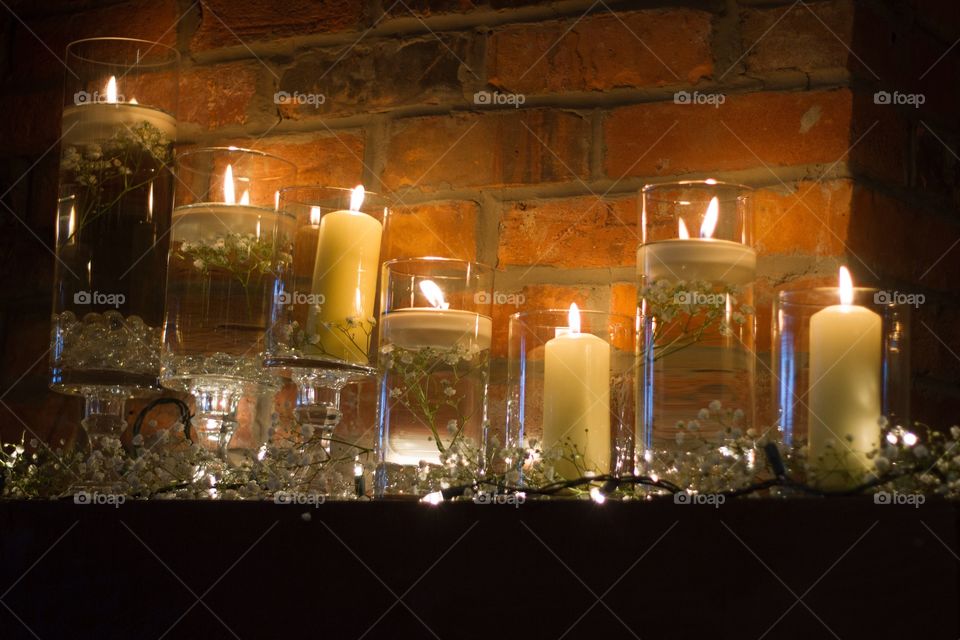A row of candles in clear cases floating with baby's breath in front of a brick wall