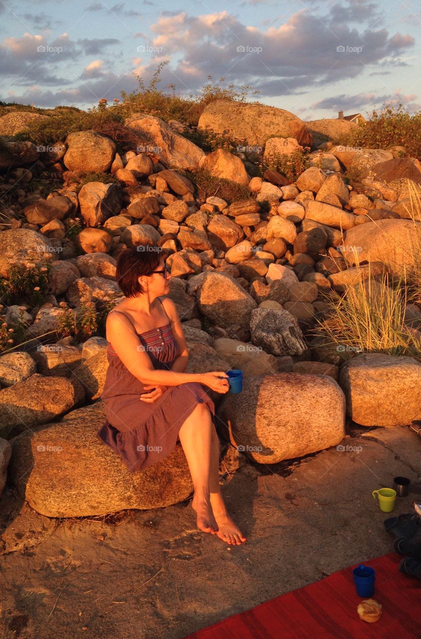 Woman sitting on rock holding cup in hand