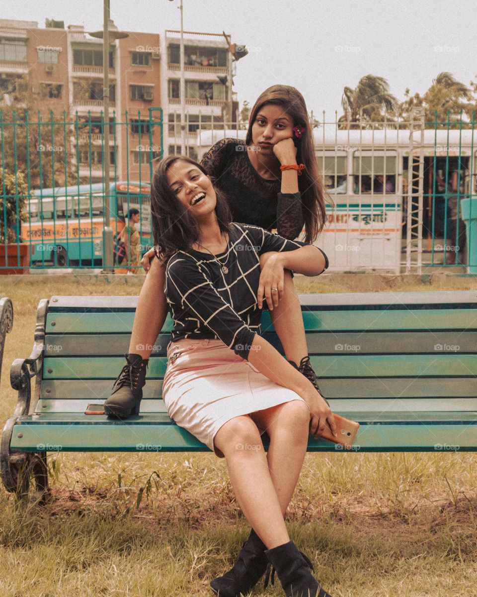 Two girls sitting on a bench depicting different moods