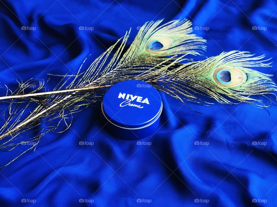 Nivea beauty face cream along with peacock feathers on blue cloth 