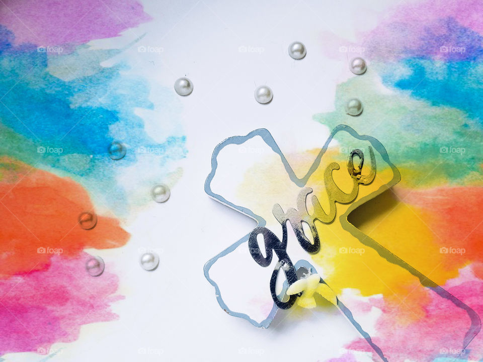 Rainbow water color background on both left and right sides, on a white background with a white cross on the right and the word grace and the cross.