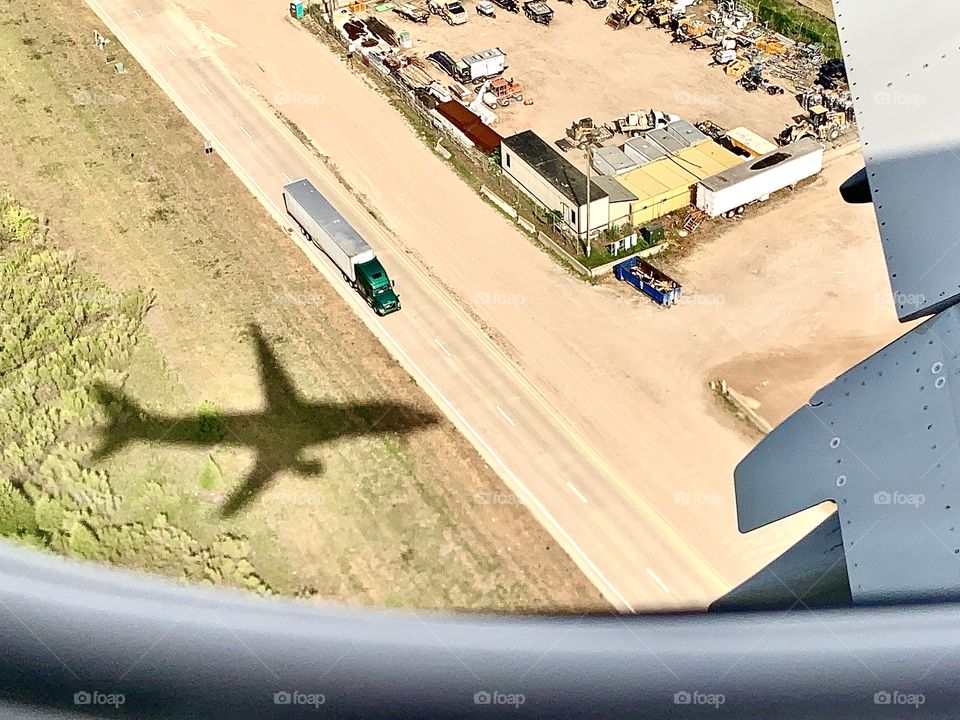 A birds eye view of the shadow of the plane I was traveling on as it approached the airport. Below I can see buildings and Sami trailer truck  as driven drive on the road on interstate 635.