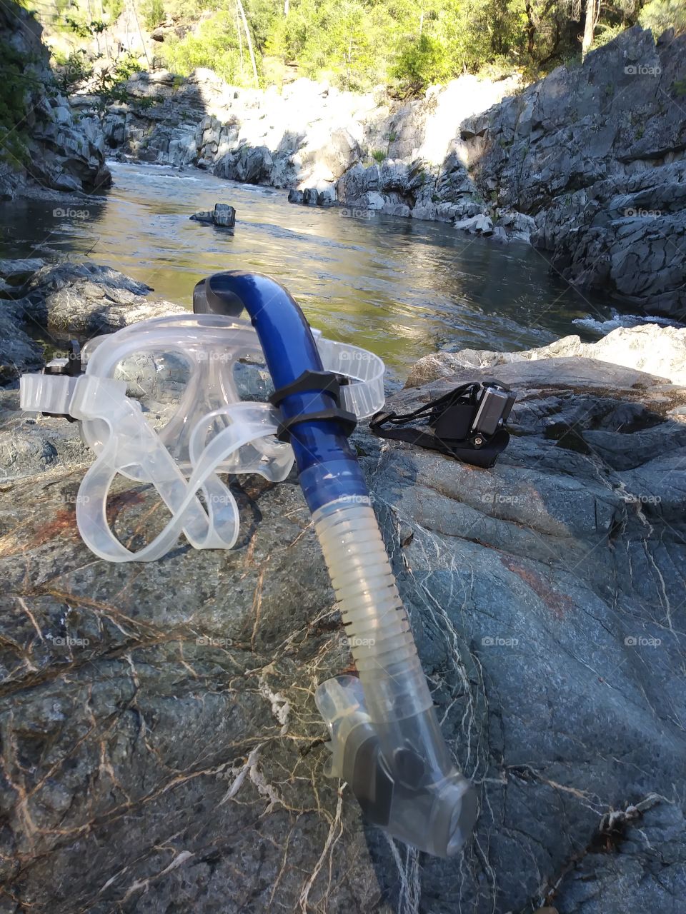 snorkel and action camera on rock by river