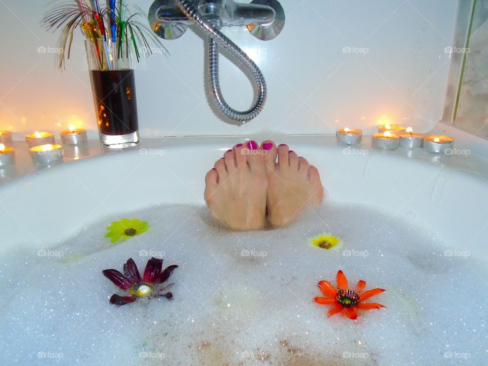 Woman's feet with red nail polish in bubble bath with candles and flowers