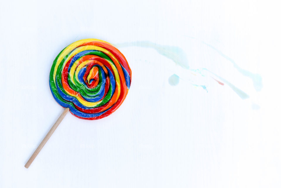 Flat lay of a large rainbow lollipop with a colorful streak on a white backdrop