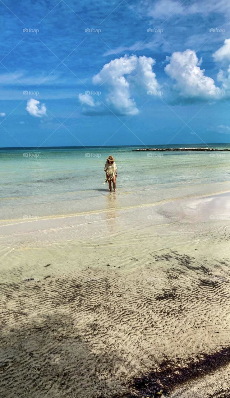 A beautiful woman wades through clear calm water on Holbox beach.