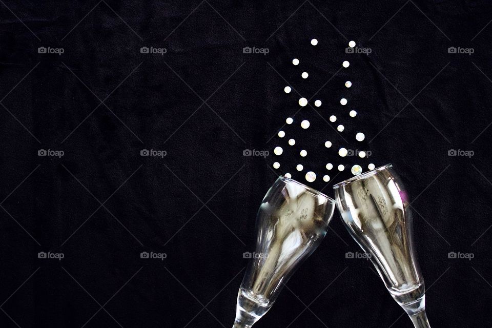 Flat lay of gleaming champagne glasses and  rhinestone bubbles on black background