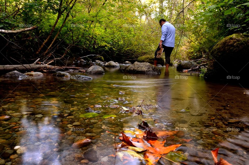 A guy in blue exploring a clean creek during autumn.