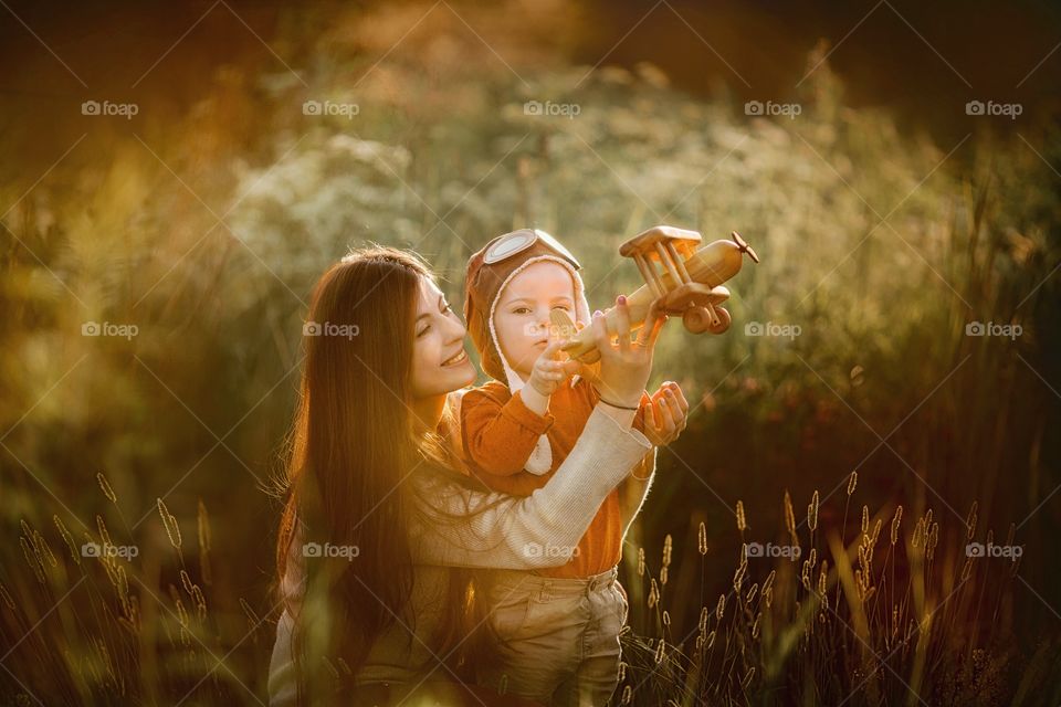 Mother with son playing with wooden plane at sunset