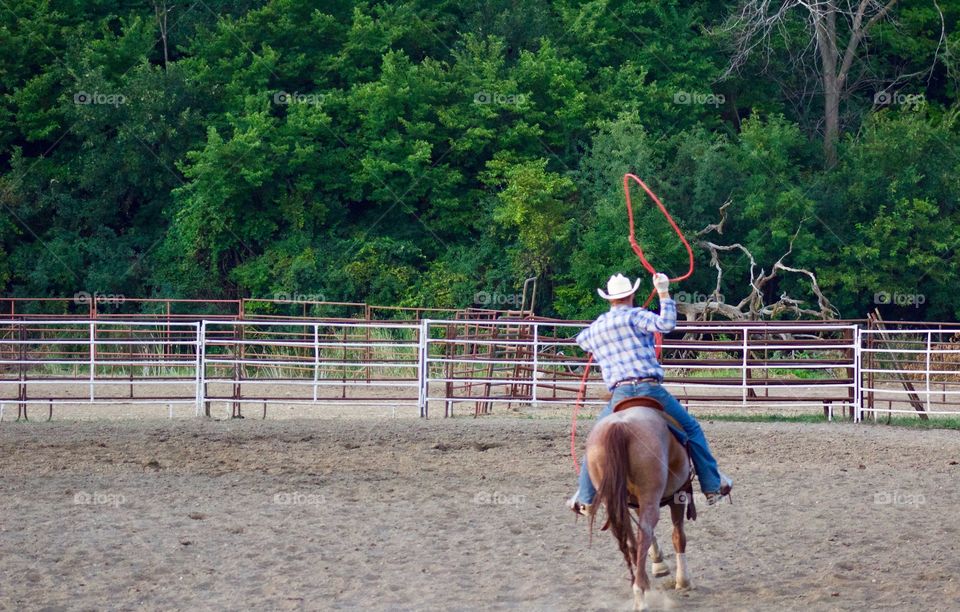 A lone rodeo rider practices with a lasso in an outdoor corral before competing 