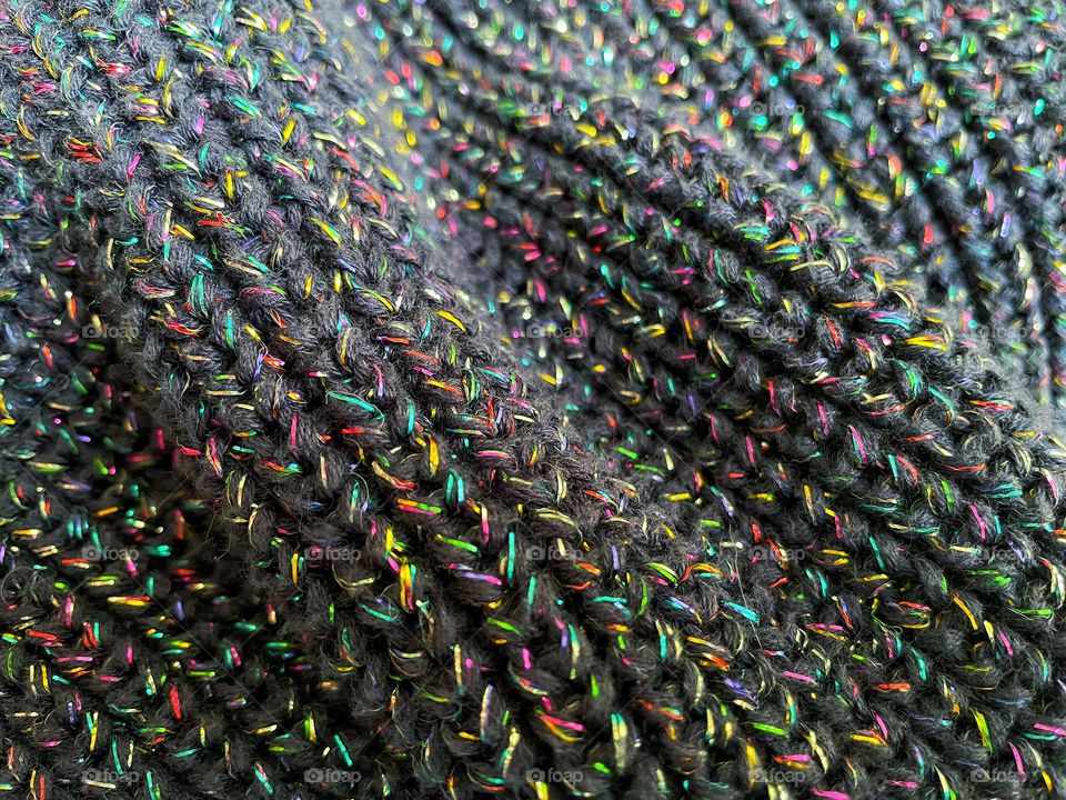 Close up knitted item with rainbow coloured metallic thread. Textured and colourful image