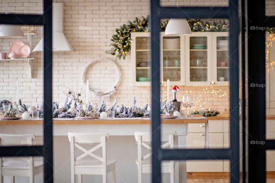 Festive winter cozy kitchen interior with garlands, decorations and gifts.  Christmas dinner at the decorated table.