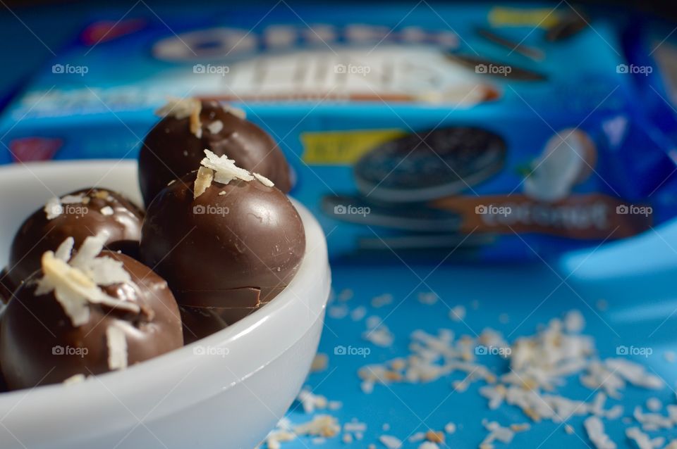 coconut Oreo thin cookies on a blue background with coconut shreds with truffles in a white bowl 