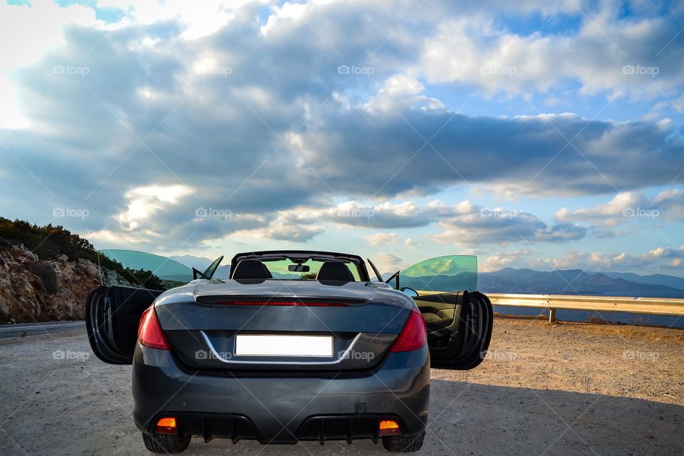 Blue convertible car on an open road on a summer day with clouds