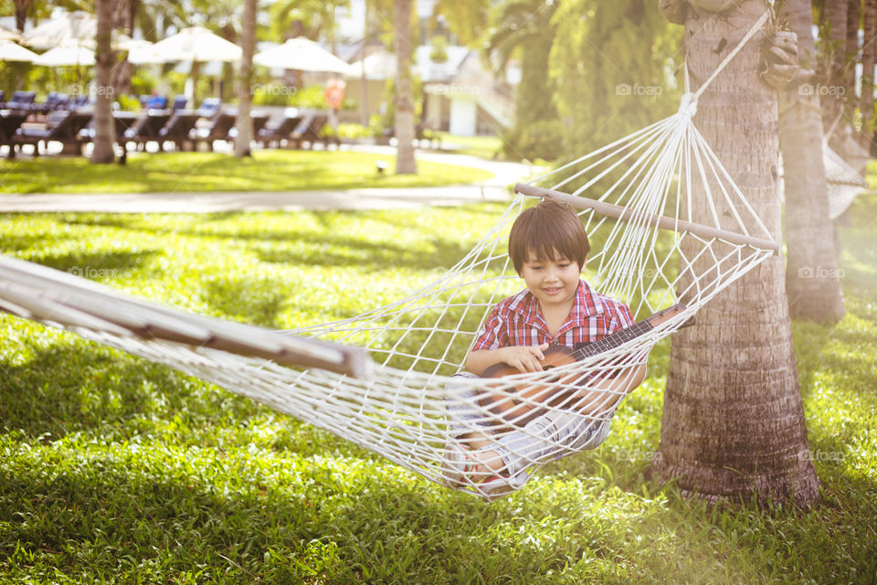 cute boy enjoying spring. Thitiwin relaxing on a hammock while playing guitar on a sunny day