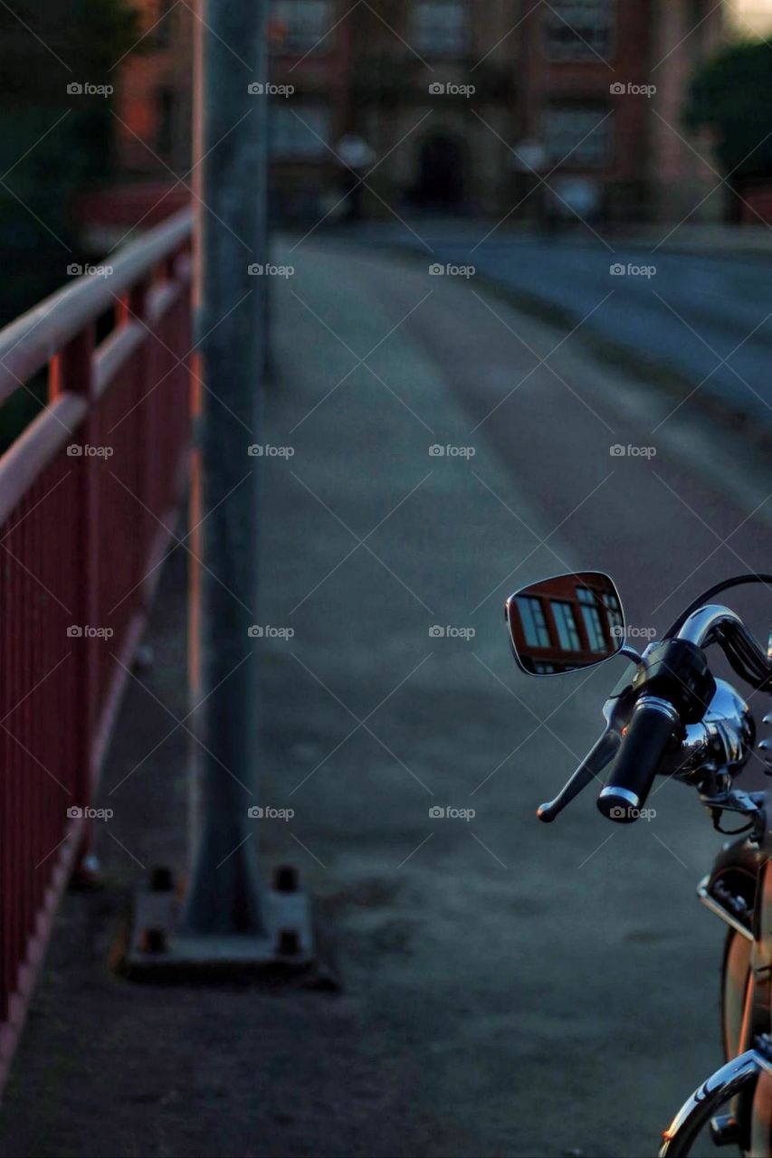 Part of a motorcycle on a bridge with red railings