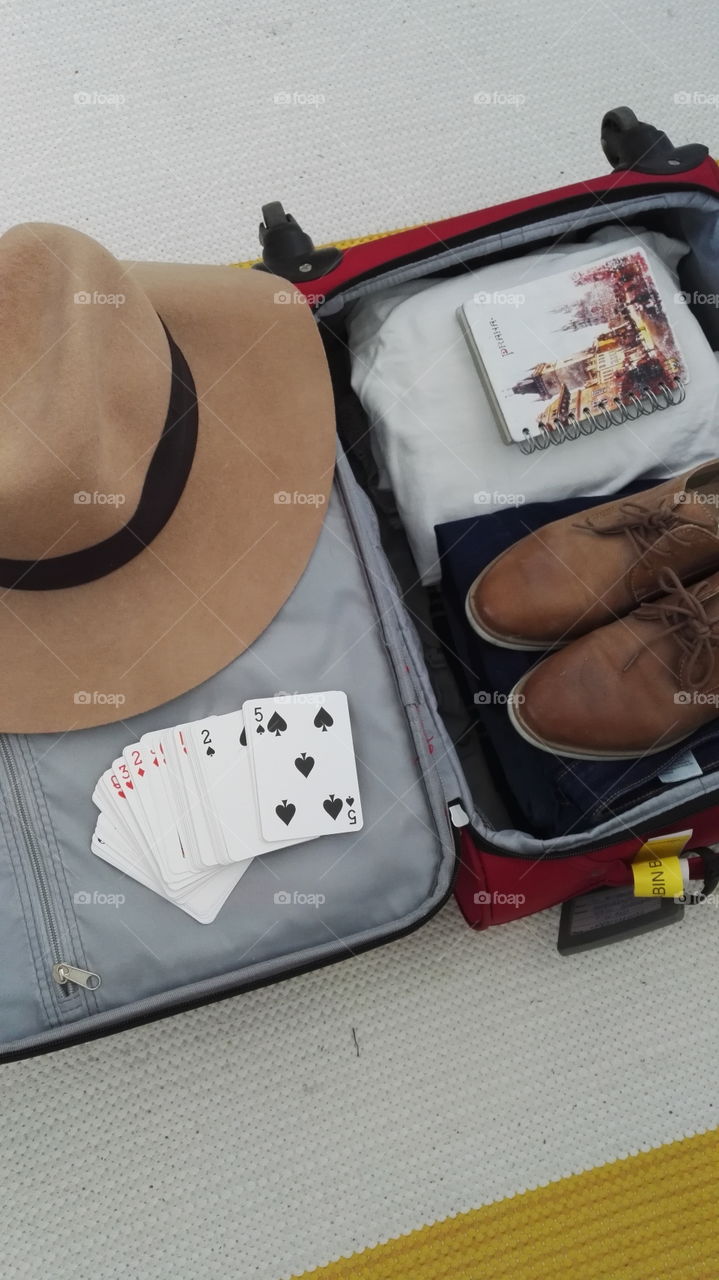 Packing simple way for a vacation. Playing cards five on top. Brown hat brown shoes white t-shirts blue jeans.