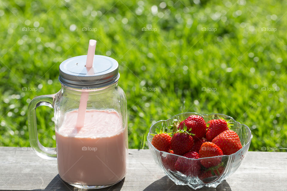 Summer, enjoying fresh strawberries and strawberry smoothie in a glass jar with lid and straw 