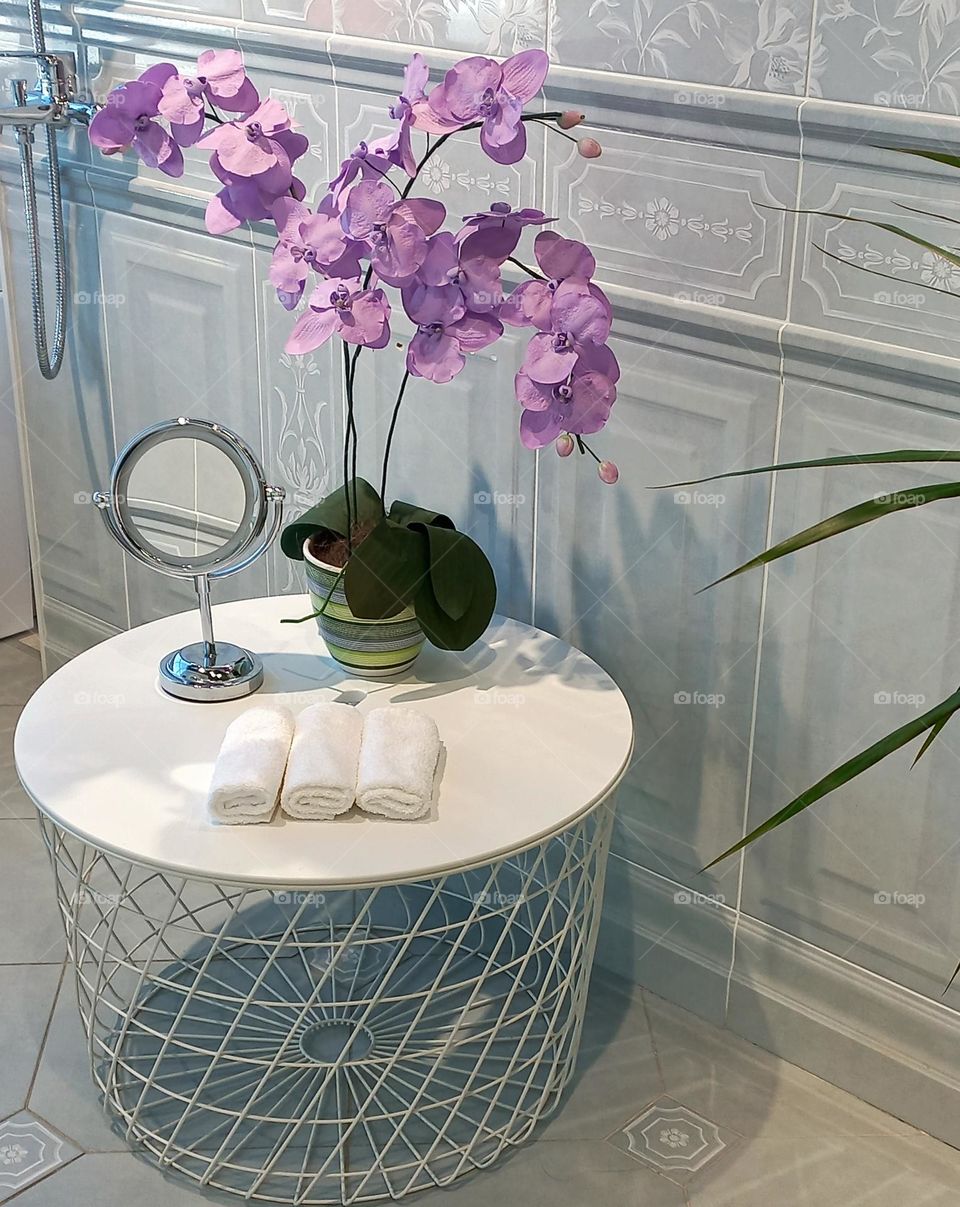minimalism in the interior of the bathroom, a bath table with an orchid flower, a mirror and towels