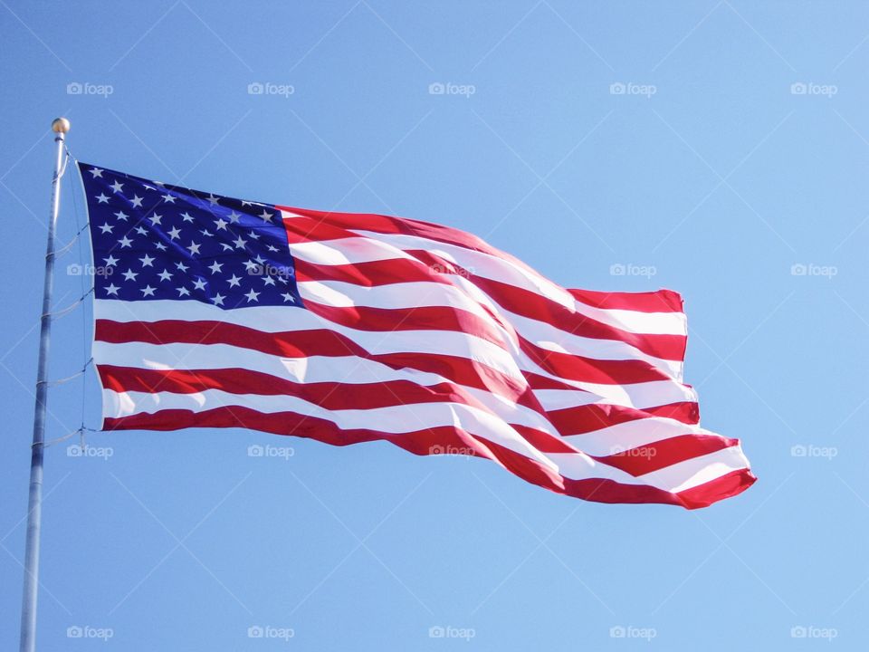 American flag of the United States flying in the wind on a bright blue sky day