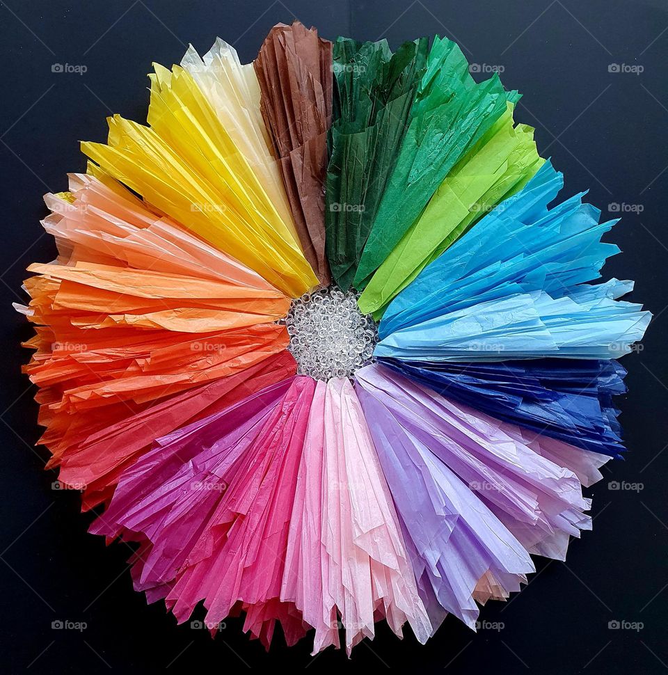 Flatlay composition of a multi-coloured flower made of silk papers and clear beads placed on black paper, creating a colour explosion