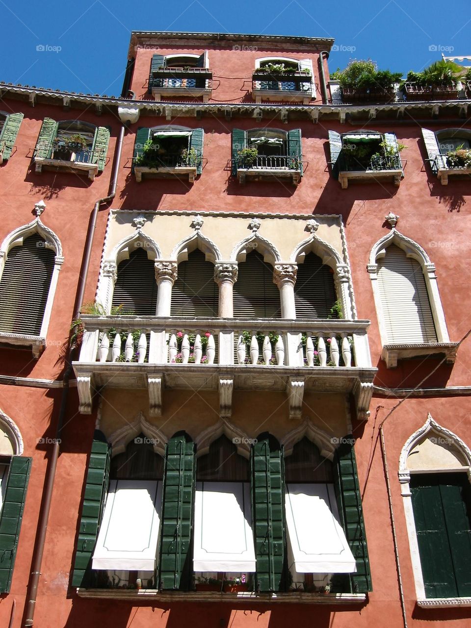 Venetian building with red exterior, ornate windows and balcony with rich blue sky above