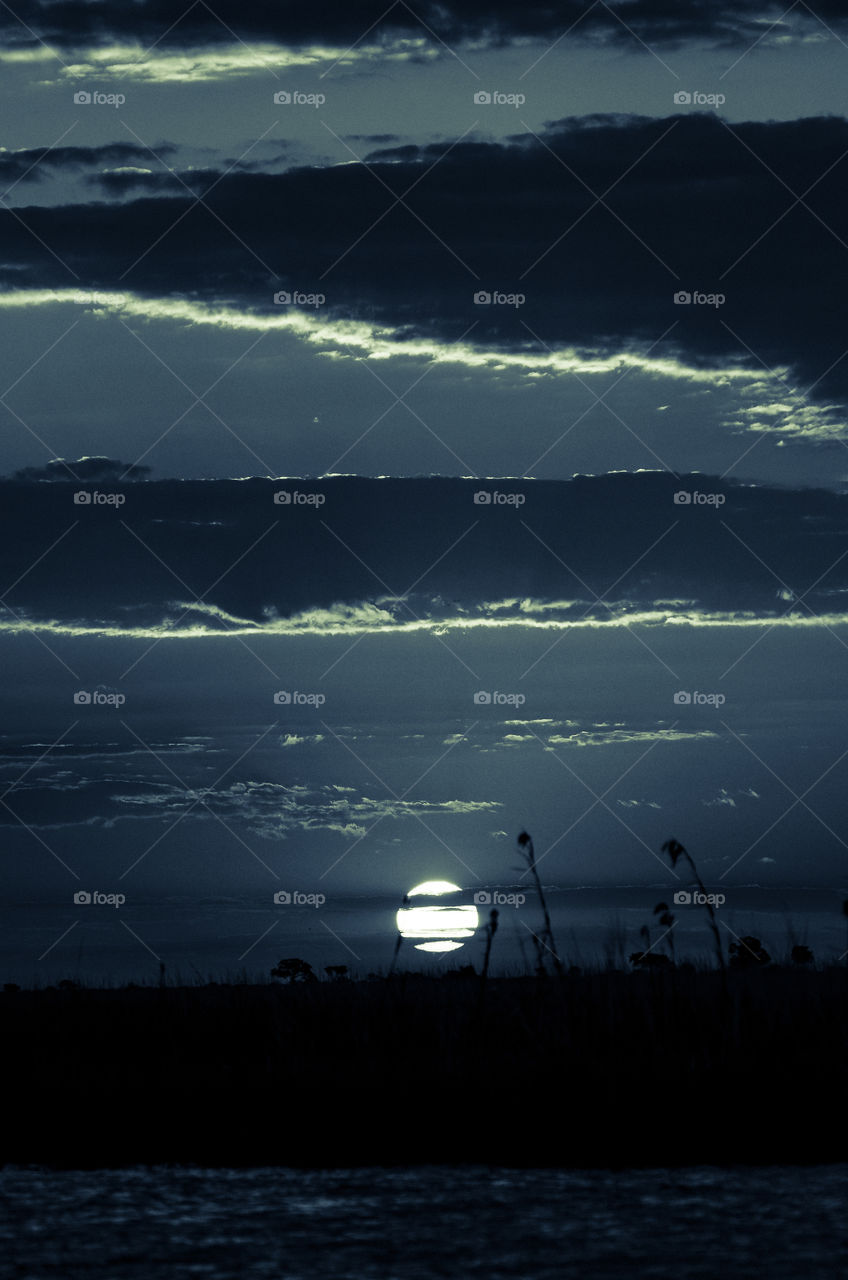 Moon through the clouds over the Chobe river with moonlight on the clouds. Beautiful African evening.