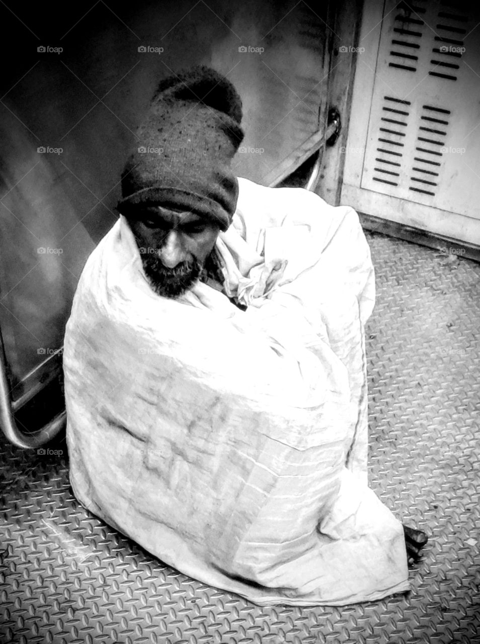 An old Homeless man covered with a thin Blanket Sleeping at the corner trying to keep himself warm in the cold.