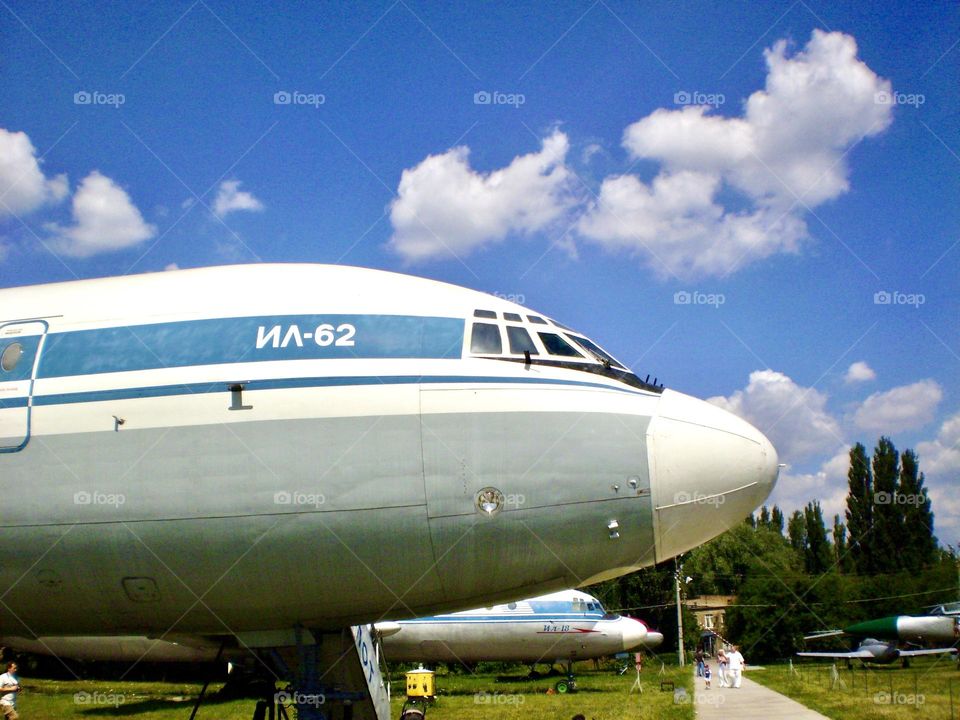 На фото изображен нос большого самолета, стоящего на земле. Самолет кажется внушительным и мощным, его обтекаемый фюзеляж блестит на солнце.
Четко видны окна кабины пилотов, слегка тонированные для защиты от яркого света.