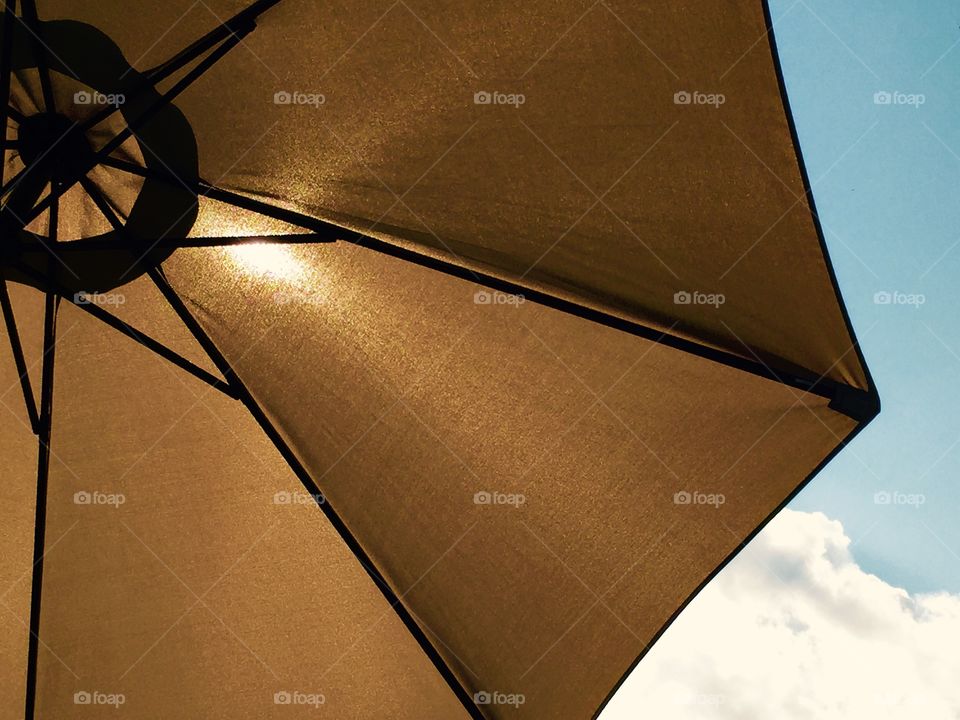 Market tan umbrella against the blue sky with the sun shinning through it. 