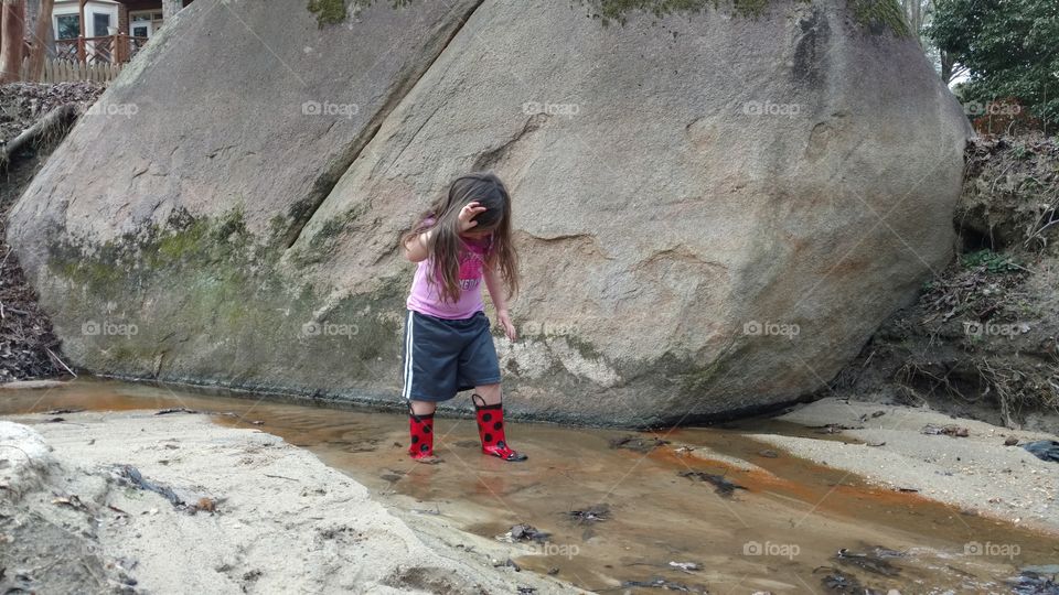 A young girl walking through a stream wearing her rain boots