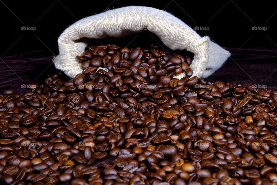 Low angle view of spilled roasted coffee beans from a burlap sack.
